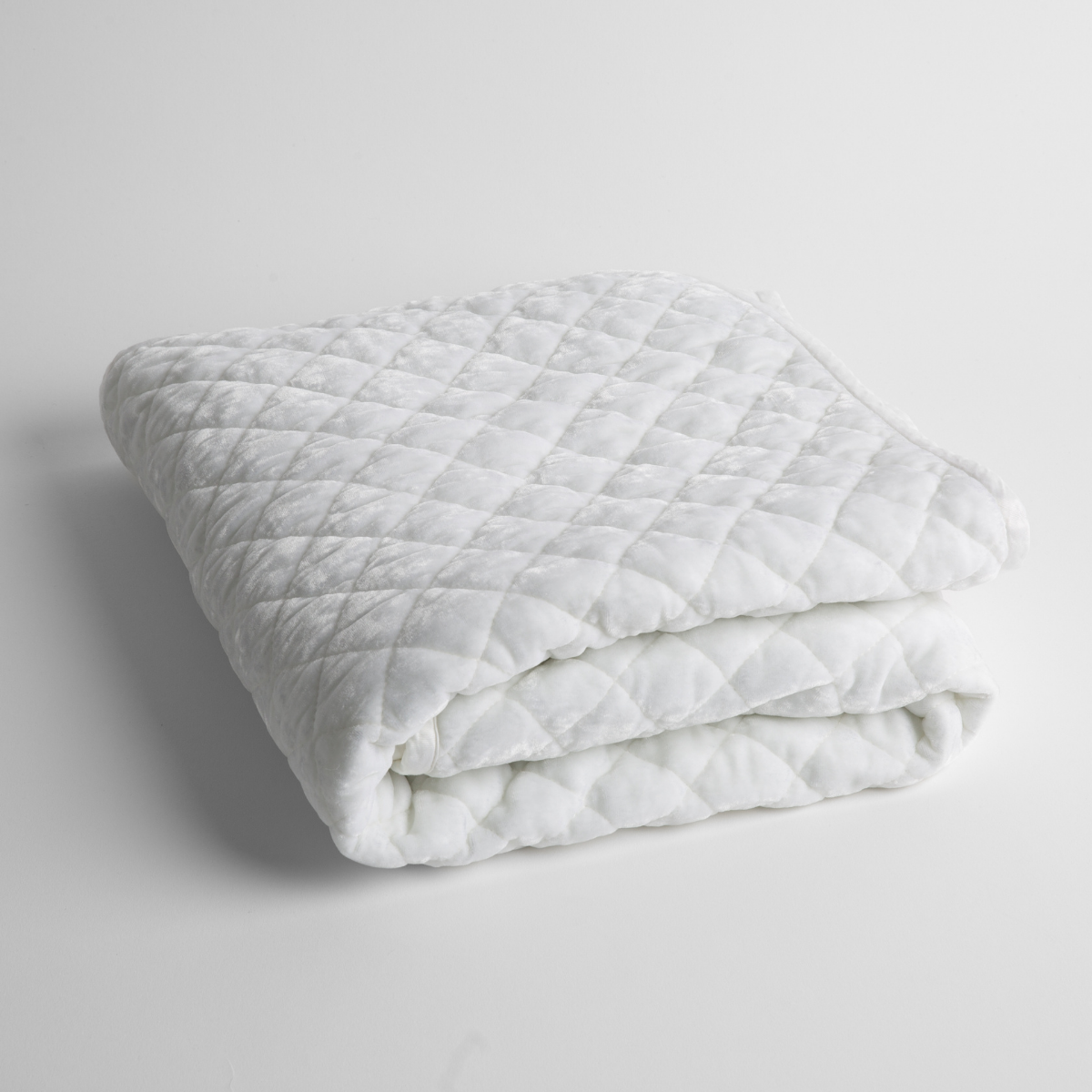 White: a folded quilted silk velvet baby blanket shown from overhead to showcase quilting pattern and texture.