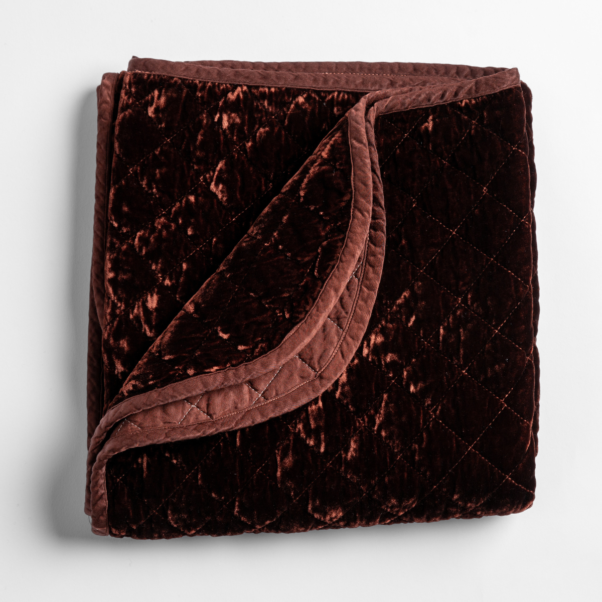 Autumn: A close-up of the corner of a folded Silk Velvet Quilted Blanket in Autumn, a rich terracotta tone, shown against a white background.