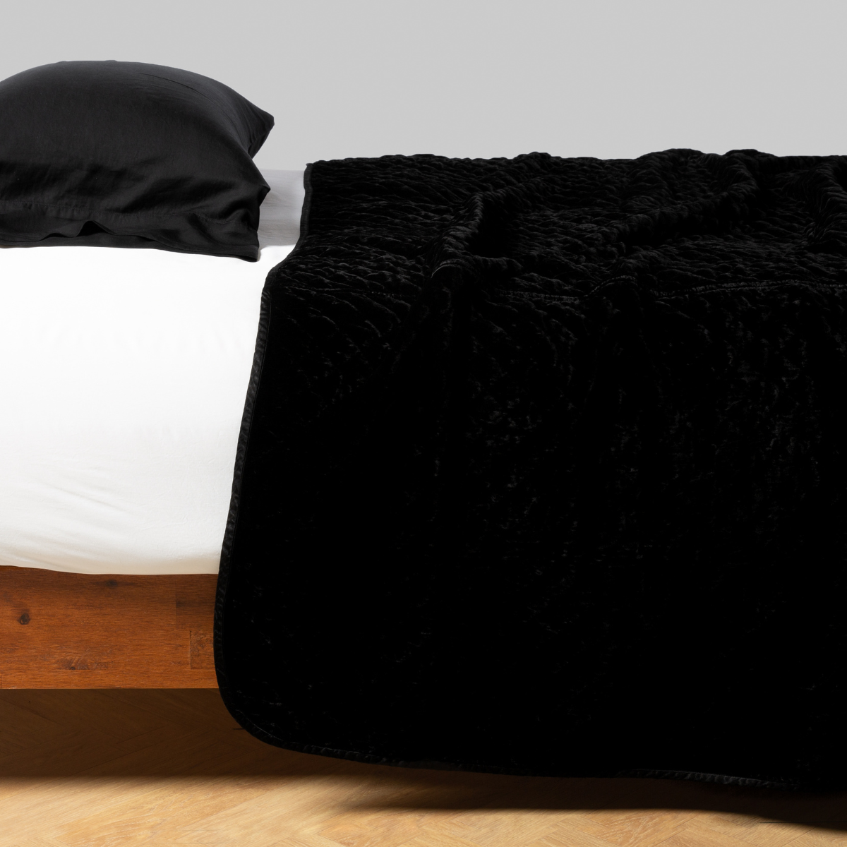 Corvino: quilted silk velvet coverlet shown from the side on a white fitted sheet with a corivno pillowcase.