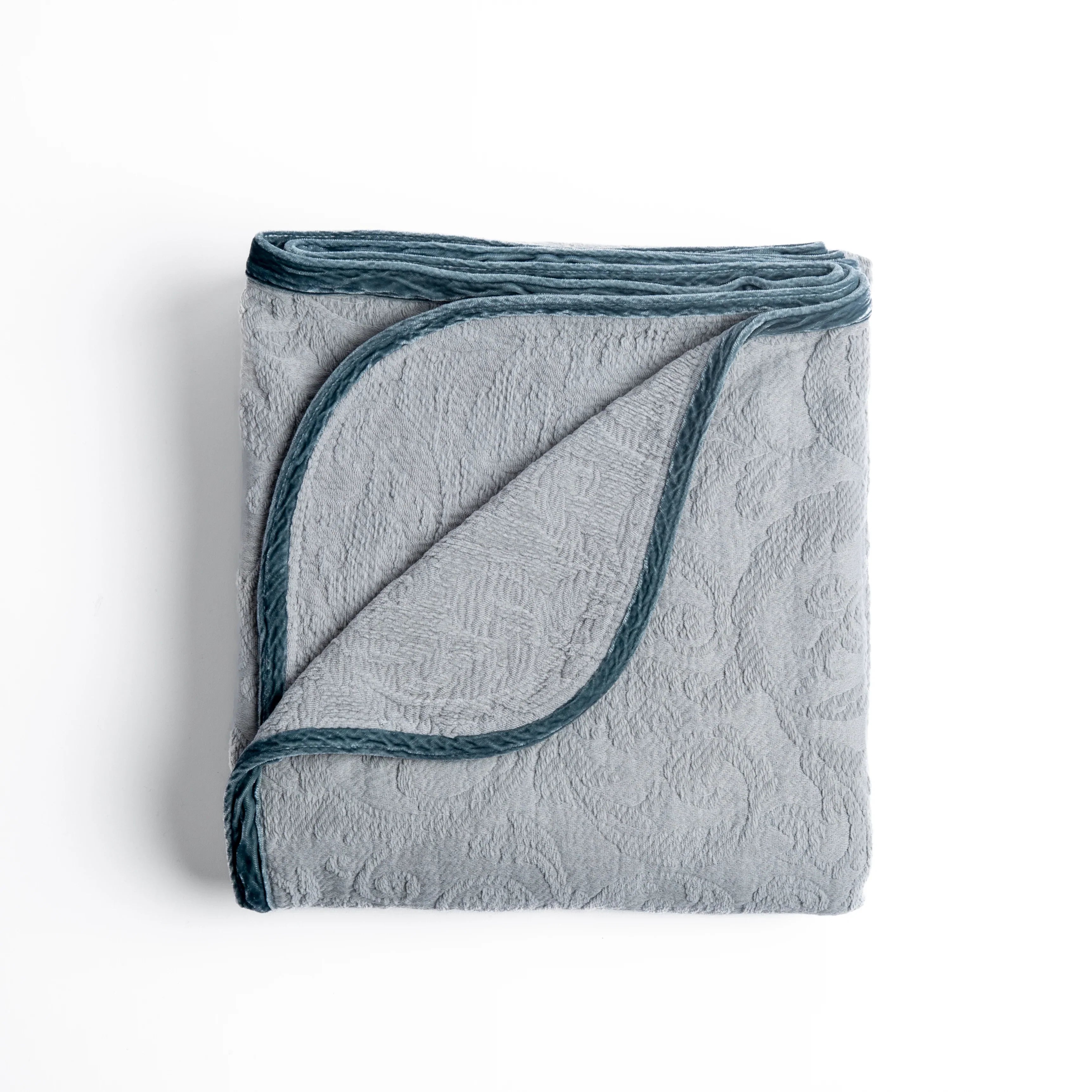 Mineral: folded organic cotton damask throw blanket shown with the corner folded down to show silk velvet trim detail β overhead against a plain white background.