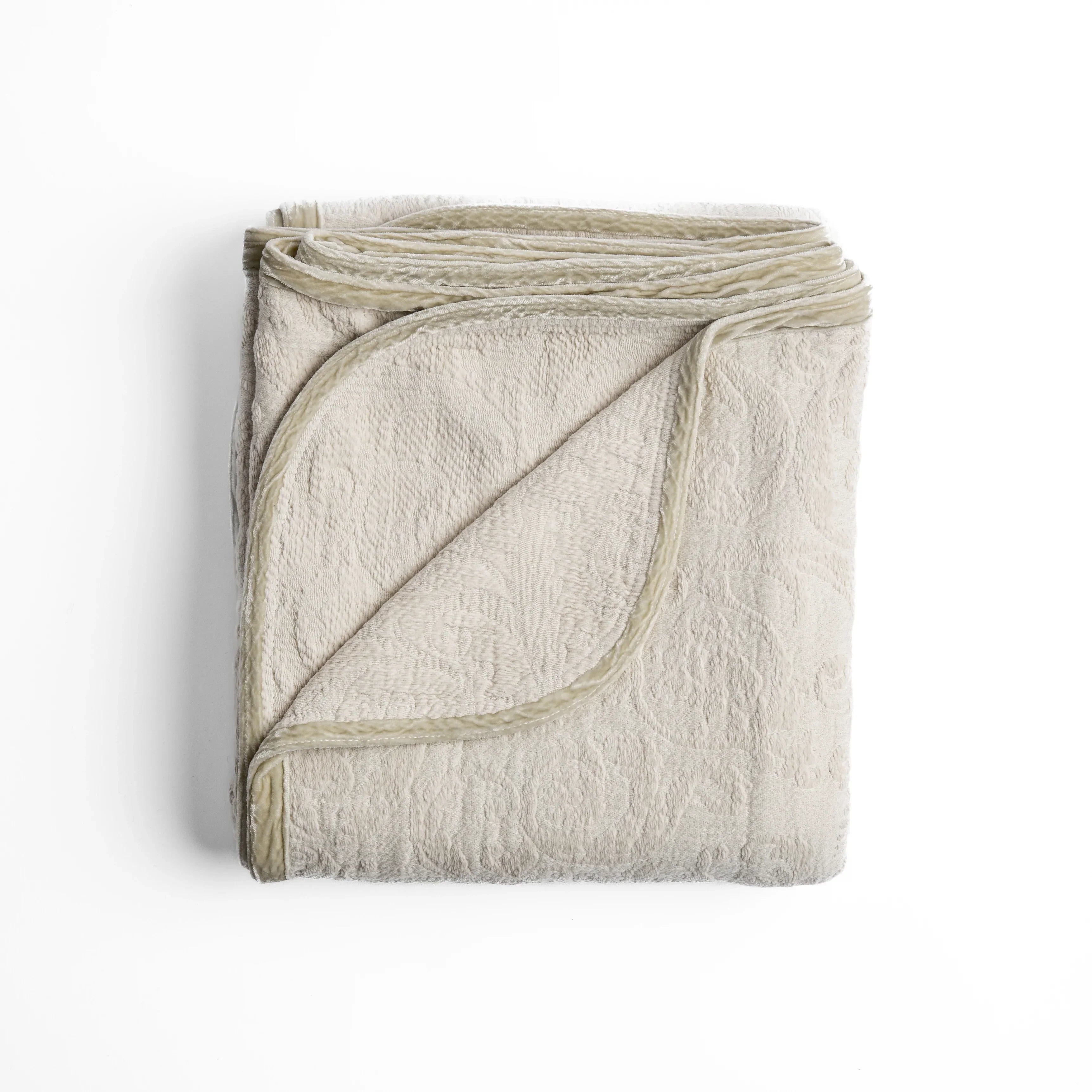 Parchment: folded organic cotton damask throw blanket shown with the corner folded down to show silk velvet trim detail β overhead against a plain white background.