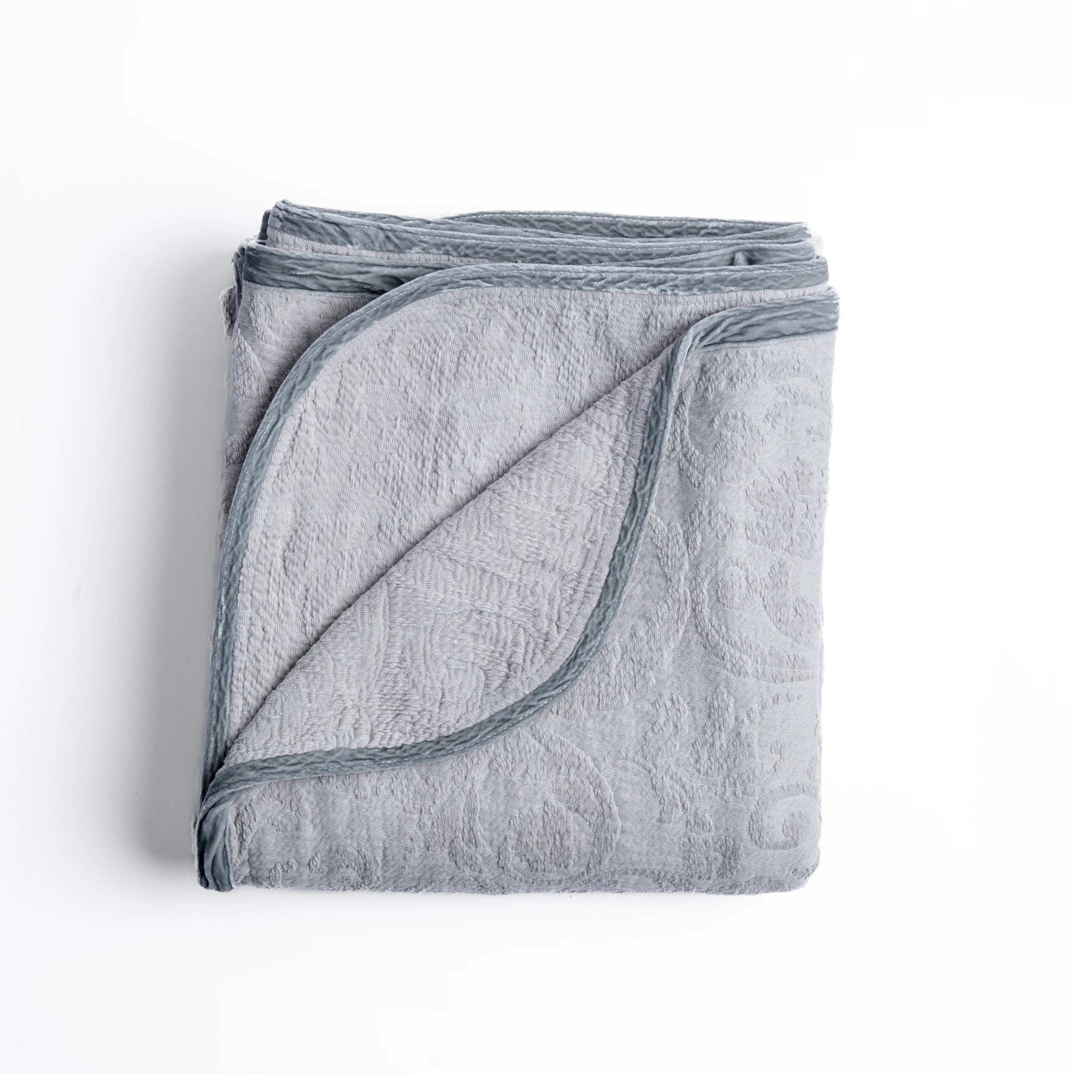 Sterling: folded organic cotton damask throw blanket shown with the corner folded down to show silk velvet trim detail β overhead against a plain white background.