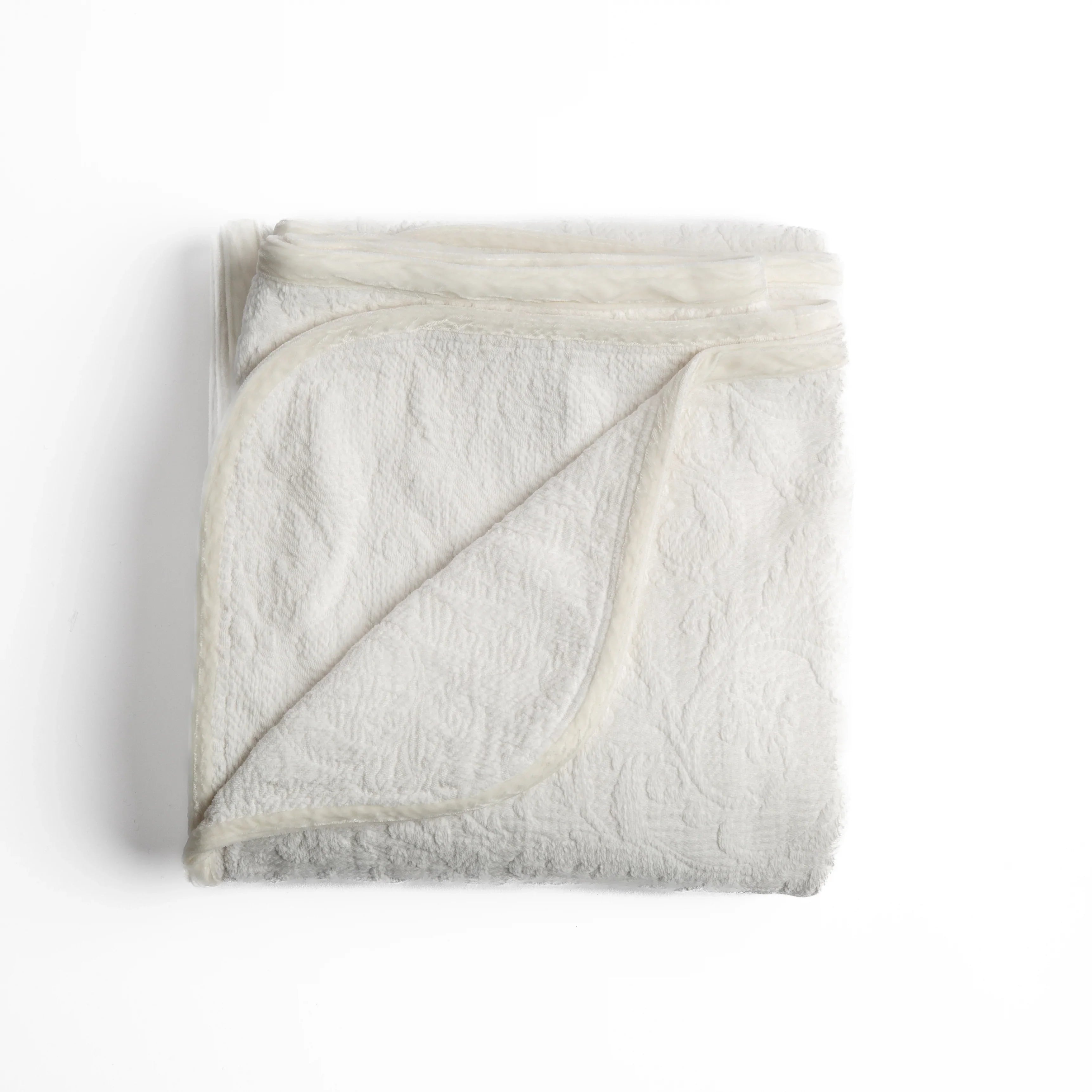 Winter White: folded organic cotton damask throw blanket shown with the corner folded down to show silk velvet trim detail β overhead against a plain white background.