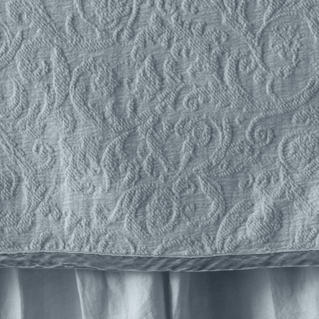 Cloud: Close up of the Adele coverlet in cloud, highlighting the detail of the cotton damask and the silk velvet edging trim. A white bed skirt peeks out at the bottom of the shot.