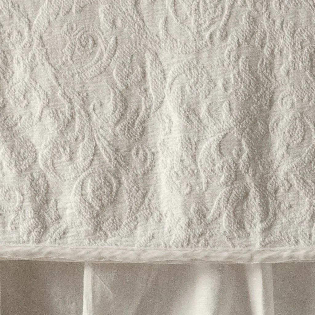 Parchment: Close up of the Adele coverlet in parchment, highlighting the detail of the cotton damask and the silk velvet edging trim. A parchment bed skirt peeks out at the bottom of the shot.