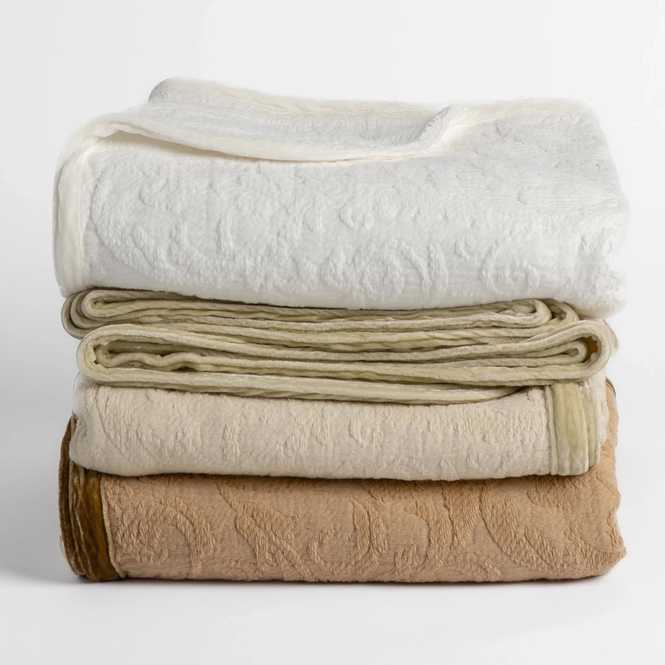 : stack of 3 organic cotton damask throw blankets in Winter White, Parchment and Honeycomb folded and shot straight on against a white background. The silk velvet trim shows textural and color contrast in each colorway shown.