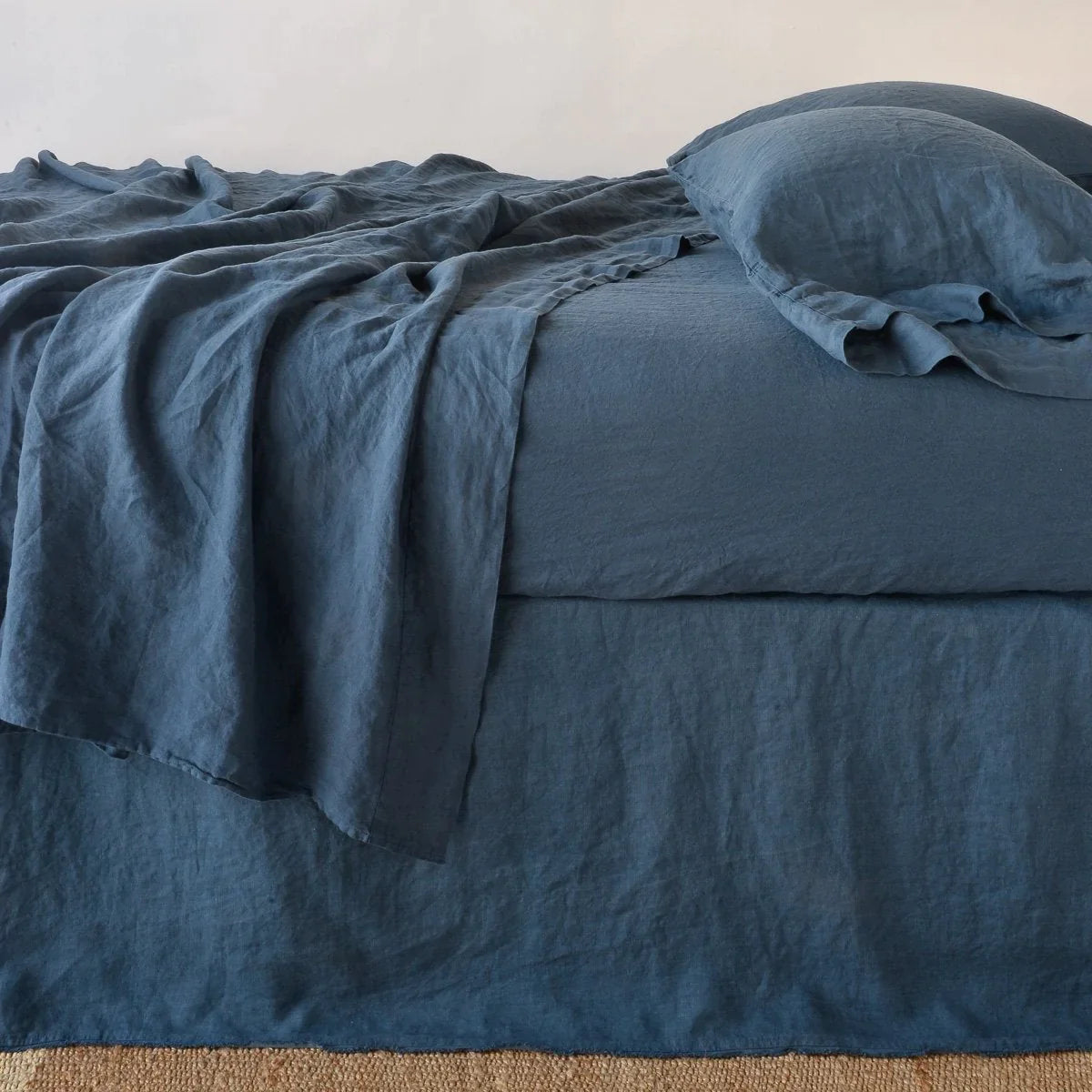: Austin bed skirt in midnight shown from the side on a bed with monochromatic sheeting, highlighting its tailored, ungathered style.