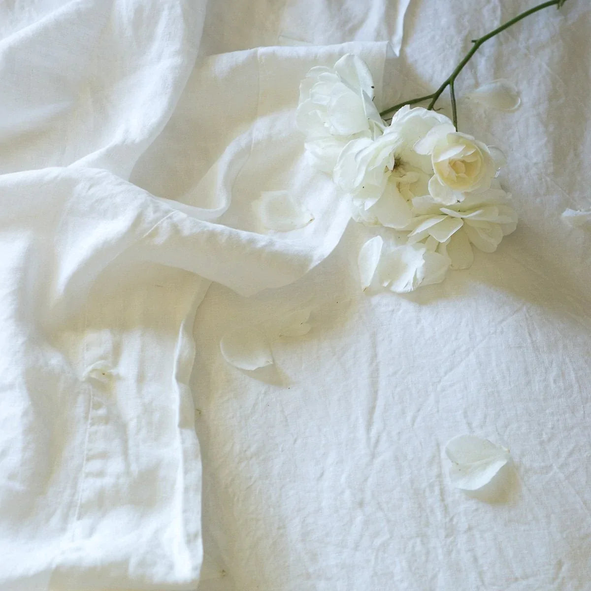 : Linen fitted and flat sheets in light cream tone with scattered white flowers and petals - overhead view.