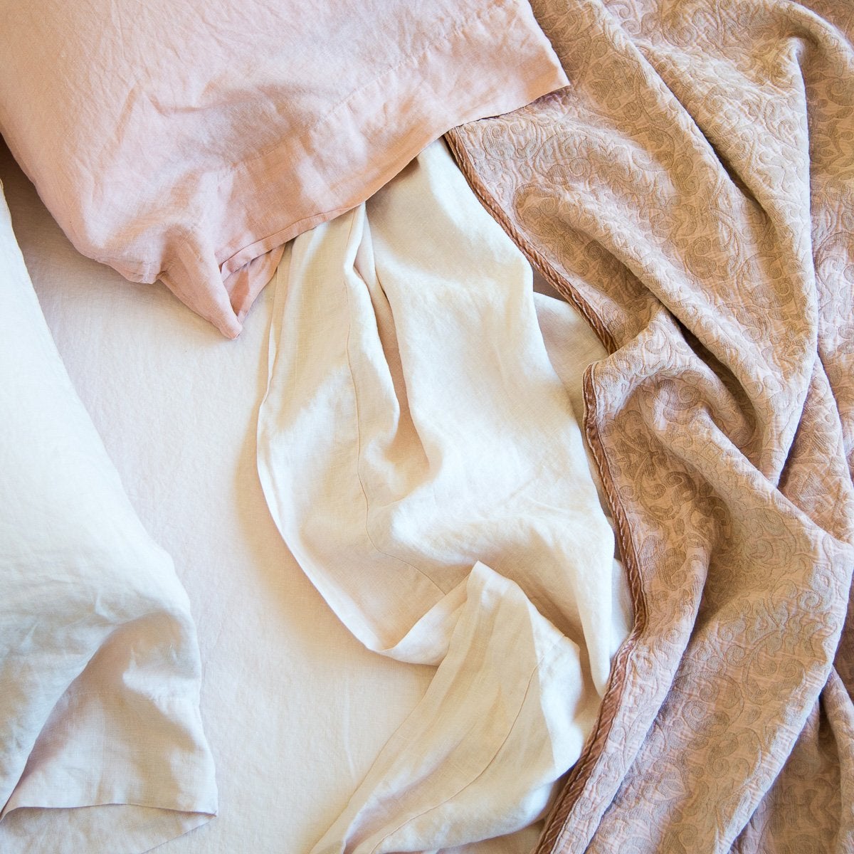 : Linen pillowcases with rumpled sheeting and Vienna cotton chenille jacquard in soft pink tones - overhead view.