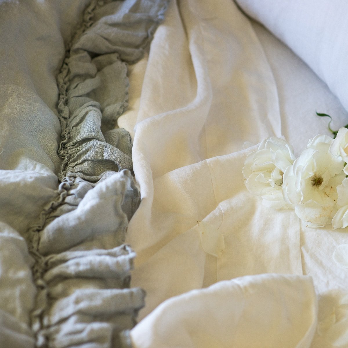 : Close-up of Linen whisper duvet cover in mineral, layered over winter white linen sheets, showcasing ruffle trim detail.