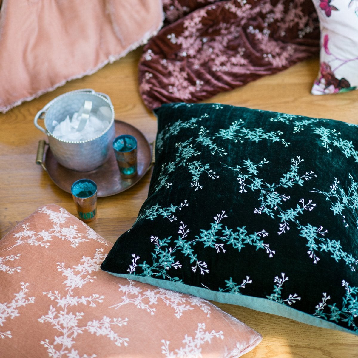 : 24x24 embroidered silk velvet pillows scattered on the floor with an ice bucket and two glasses on a small tray.