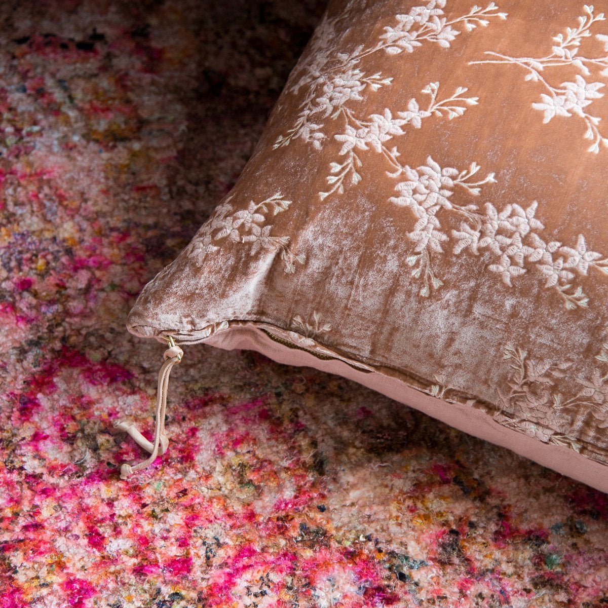 : Lynette 24 by 24 pillow in rouge on a brightly patterned rug. Close-up angle shows brass zipper, charmeuse pull, and hints at linen back.