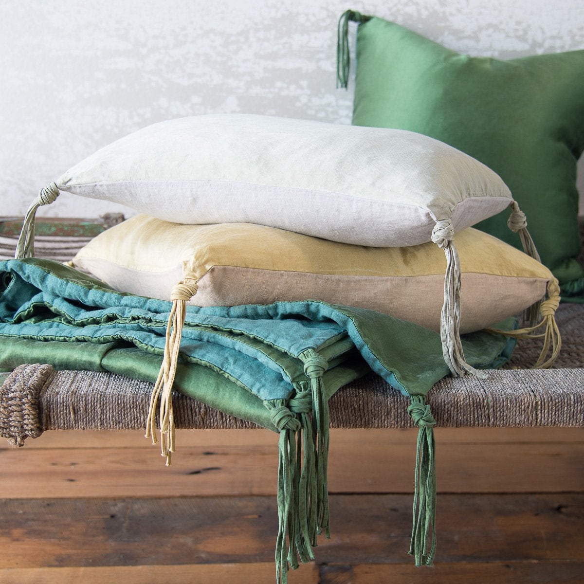 : A stack of angled Taline throw pillows on a neatly folded blanket, highlightling hand-tied tassel detail - side view.