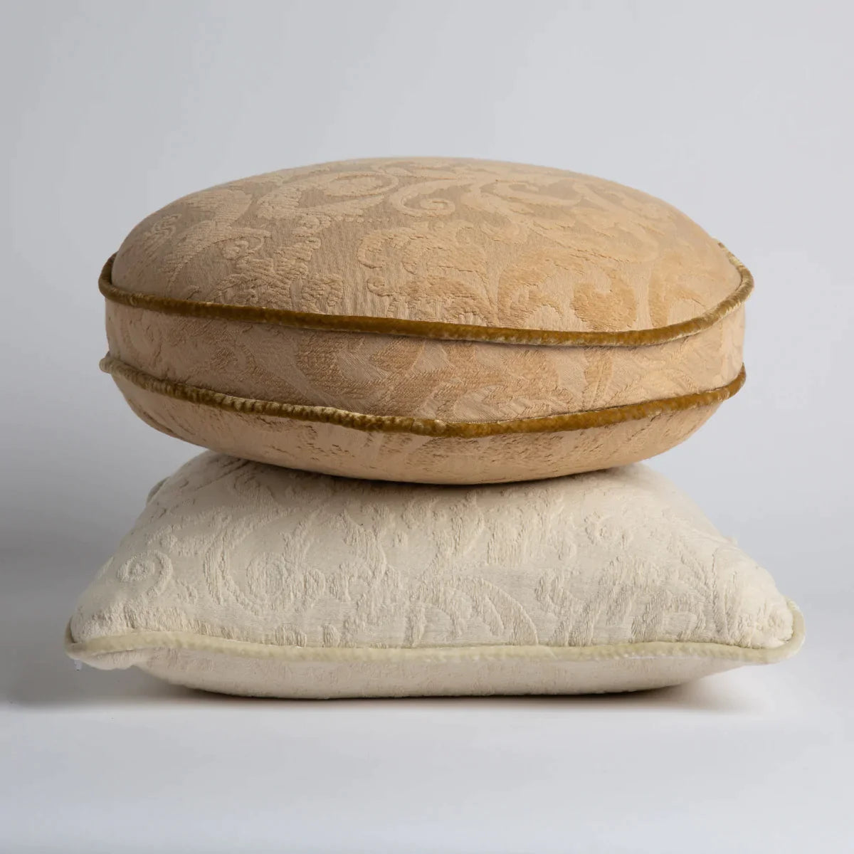 : Organic cotton damask throw pillows stacked with round pillow in honeycomb on top of square pillow in parchment.