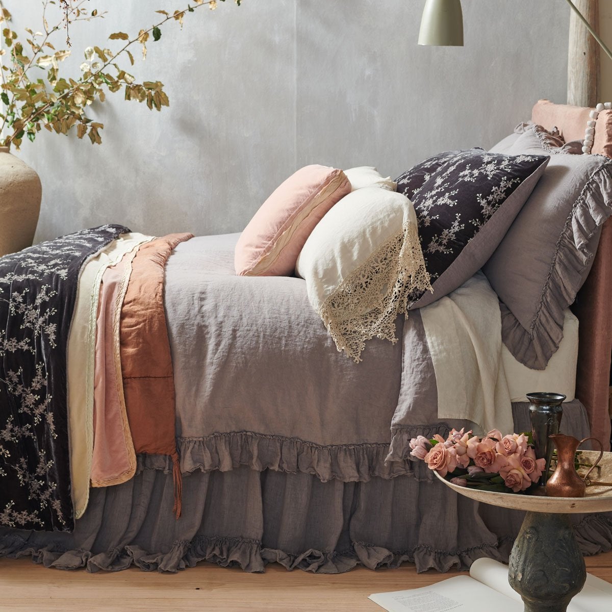 : Linen Whisper duvet cover in moonlight, shown with matching bed skirt and shams, and layered with accessory pieces in rouge and parchment - side view.