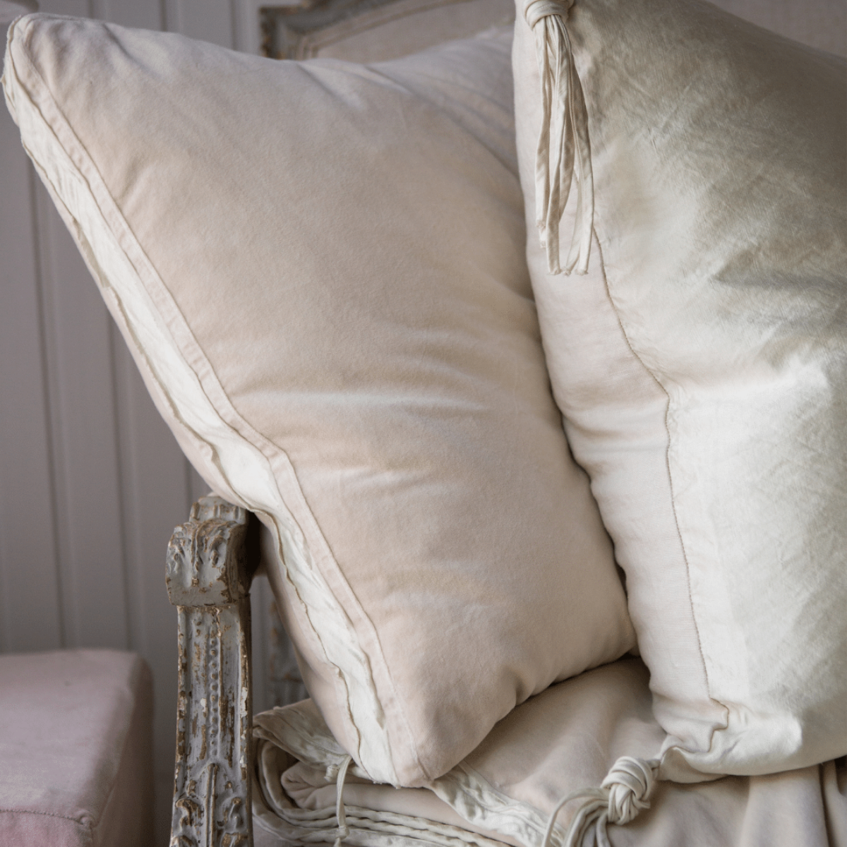 : Close up of Harlow 24 by 24 pillow, arranged on an antique sofa with complementary textures of linen and charmeuse, all in parchment.