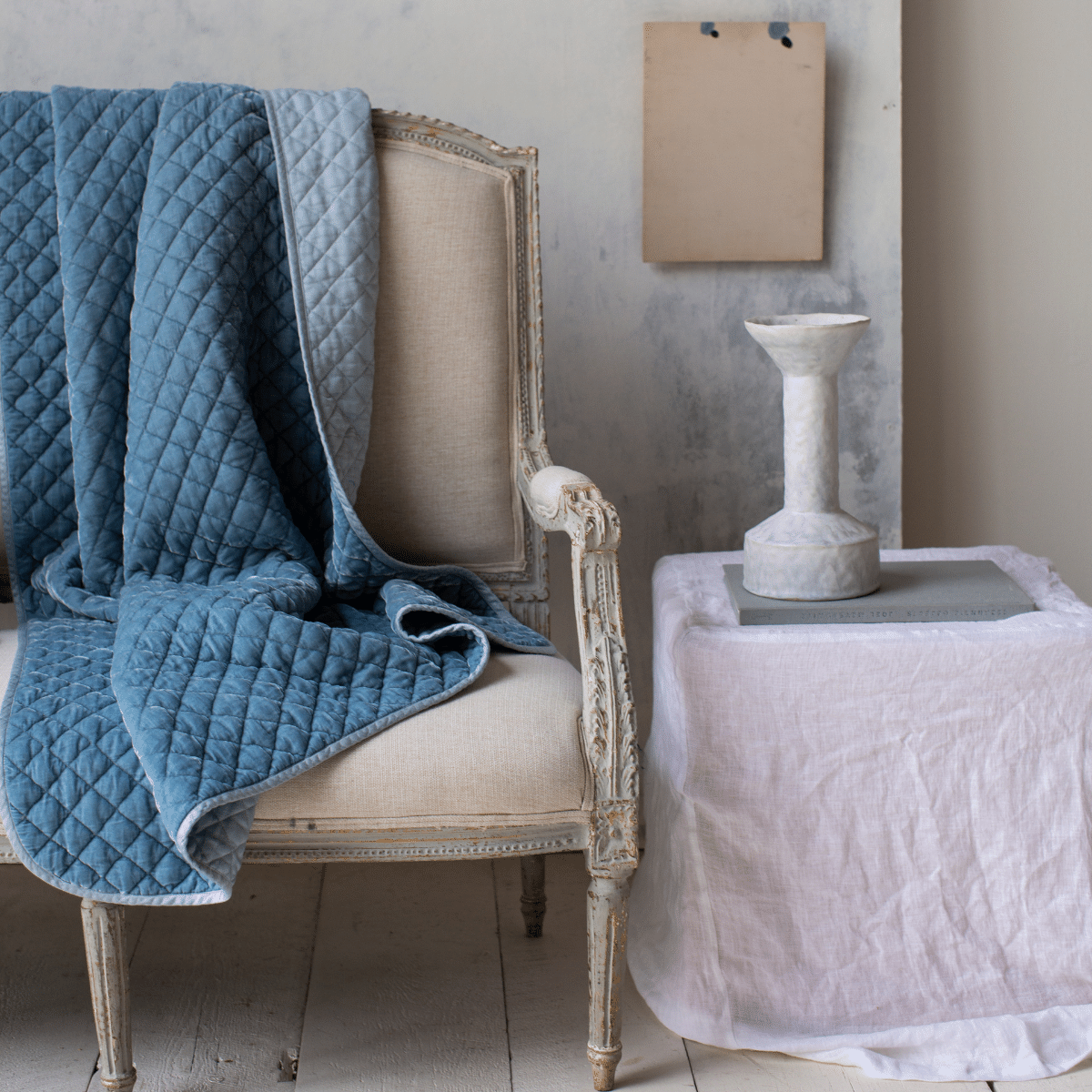 : Silk velvet quilted throw blanket in cloud, draped over a light neutral antique couch. The blanket is rumpled, showing the satin back - cropped view.