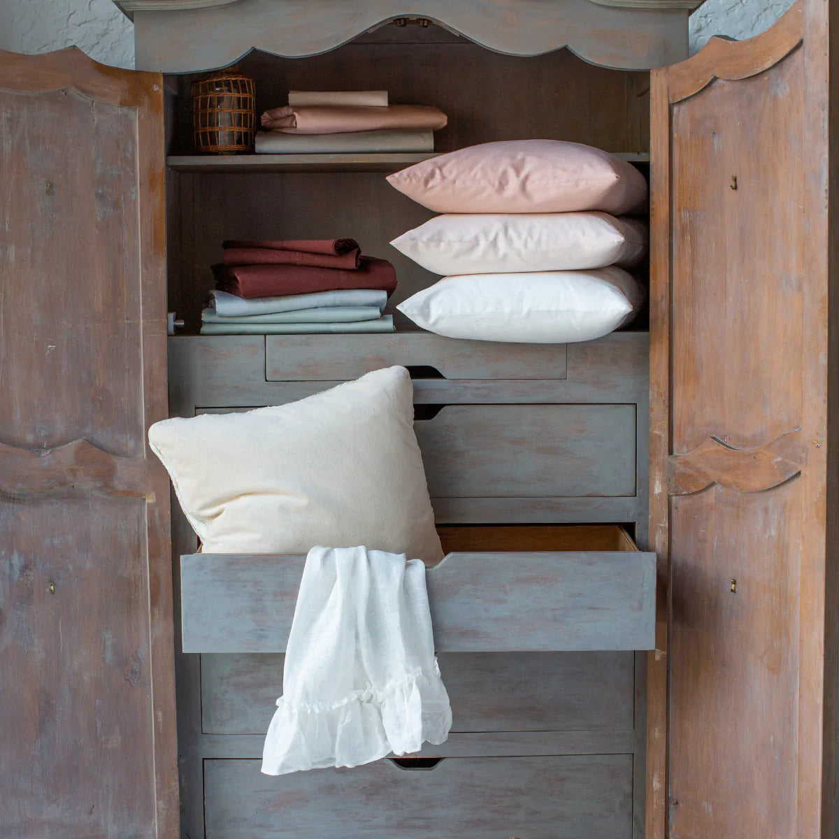 : Bria sheets and pillow cases stacked inside an antique armoire in a variety of colors.