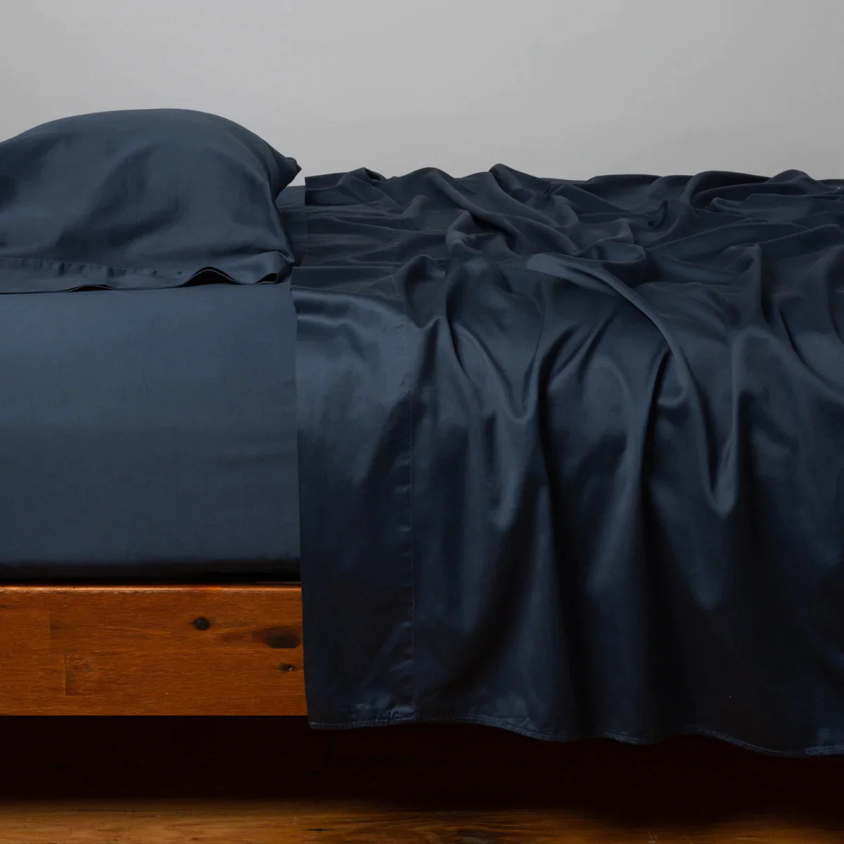 Midnight: Cotton sateen fitted sheet shown with matching flat sheet and sleeping pillow - side view.