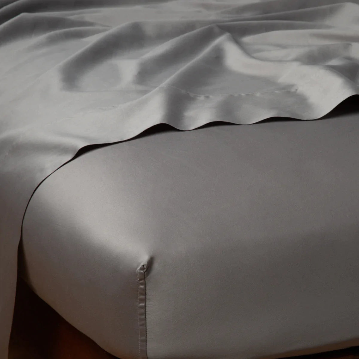 Moonlight: Cotton sateen flat sheet draped over matching fitted sheet. Shown from the top corner, the flat sheet is rumpled, highlighting the shine of the fabric.