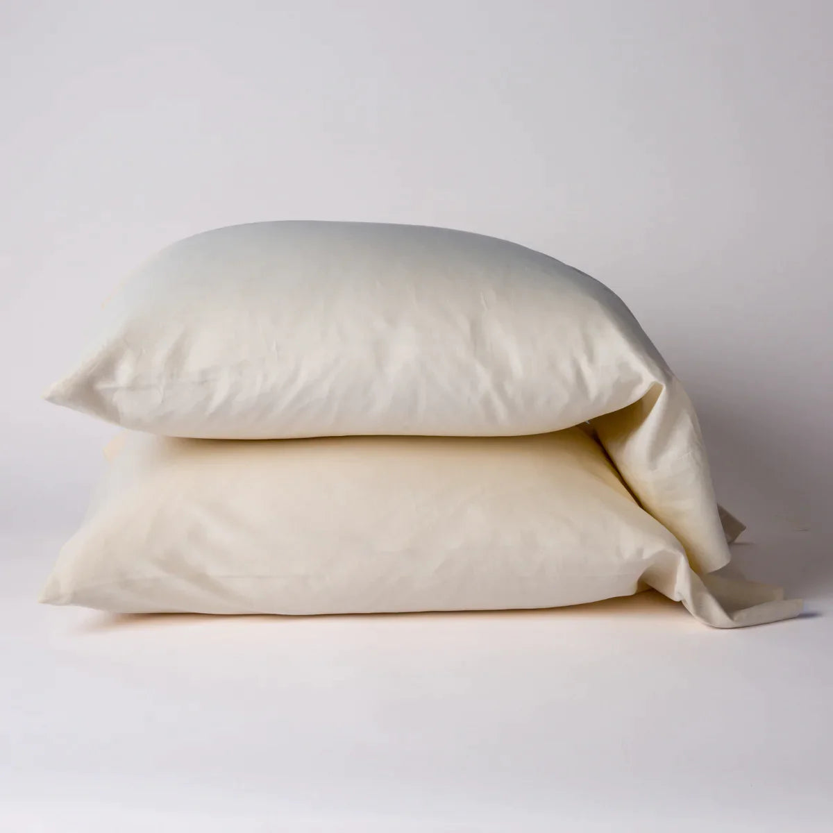 Parchment: Two cotton sateen sleeping pillows, stacked neatly against a white backdrop - side view.