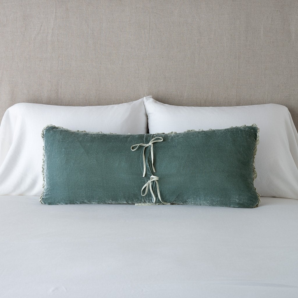 Eucalyptus: Silk velvet lumbar pillow with petite ruffle leaning upright and backwards against neutral bedding and headboard, showcaseing the silk charmeuse tie closures.