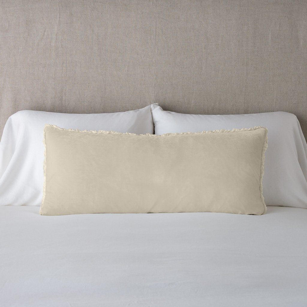 Parchment: Silk velvet lumbar pillow with petite ruffle, leaning upright against neutral bedding and headboard.