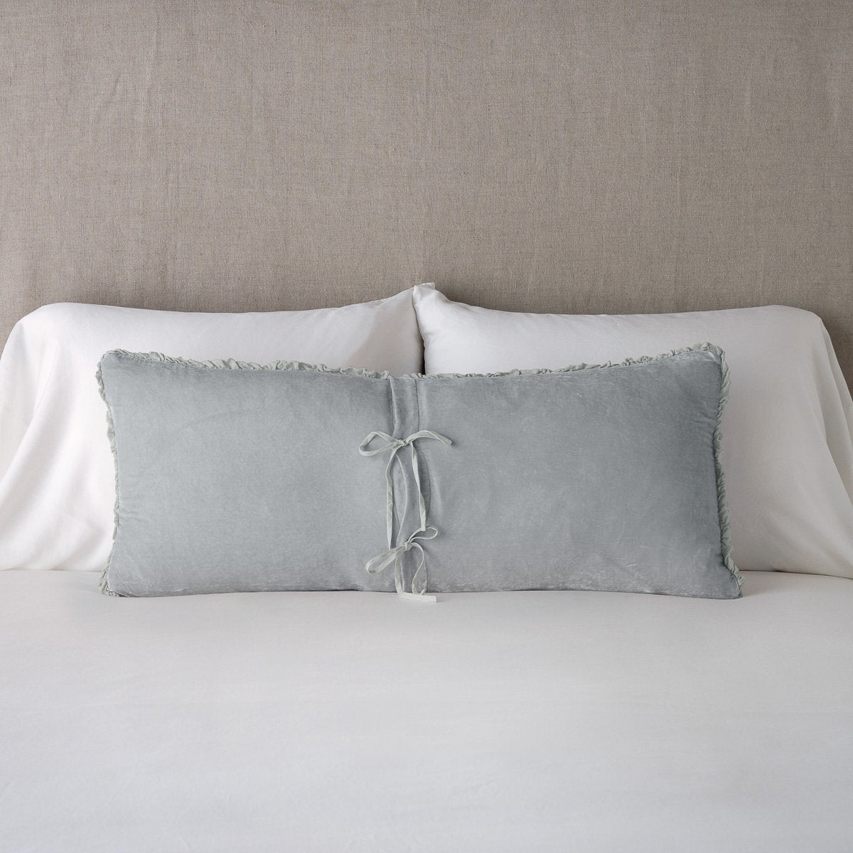 Sterling: Silk velvet lumbar pillow with petite ruffle leaning upright and backwards against neutral bedding and headboard, showcaseing the silk charmeuse tie closures.