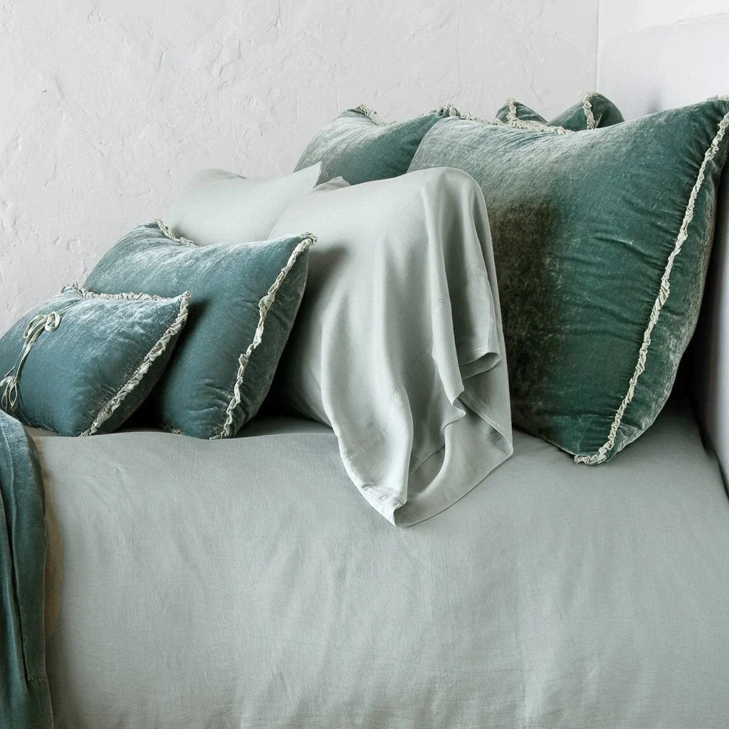 Eucalyptus: Silk velvet shams with a petite ruffle on monochromatic bed, leaning upright behind sleeping and throw pillows - side view.