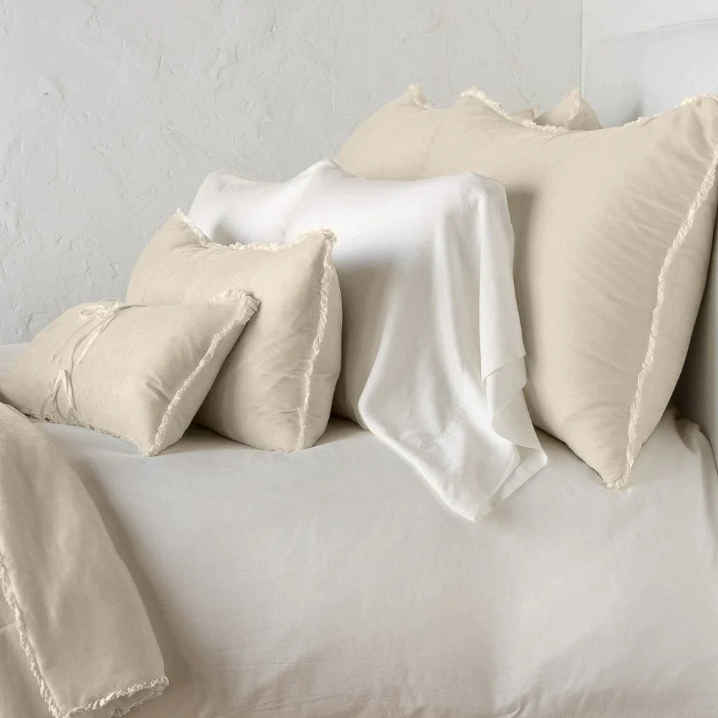 Parchment: Silk velvet shams with a petite ruffle on monochromatic bed, leaning upright behind sleeping and throw pillows - side view.