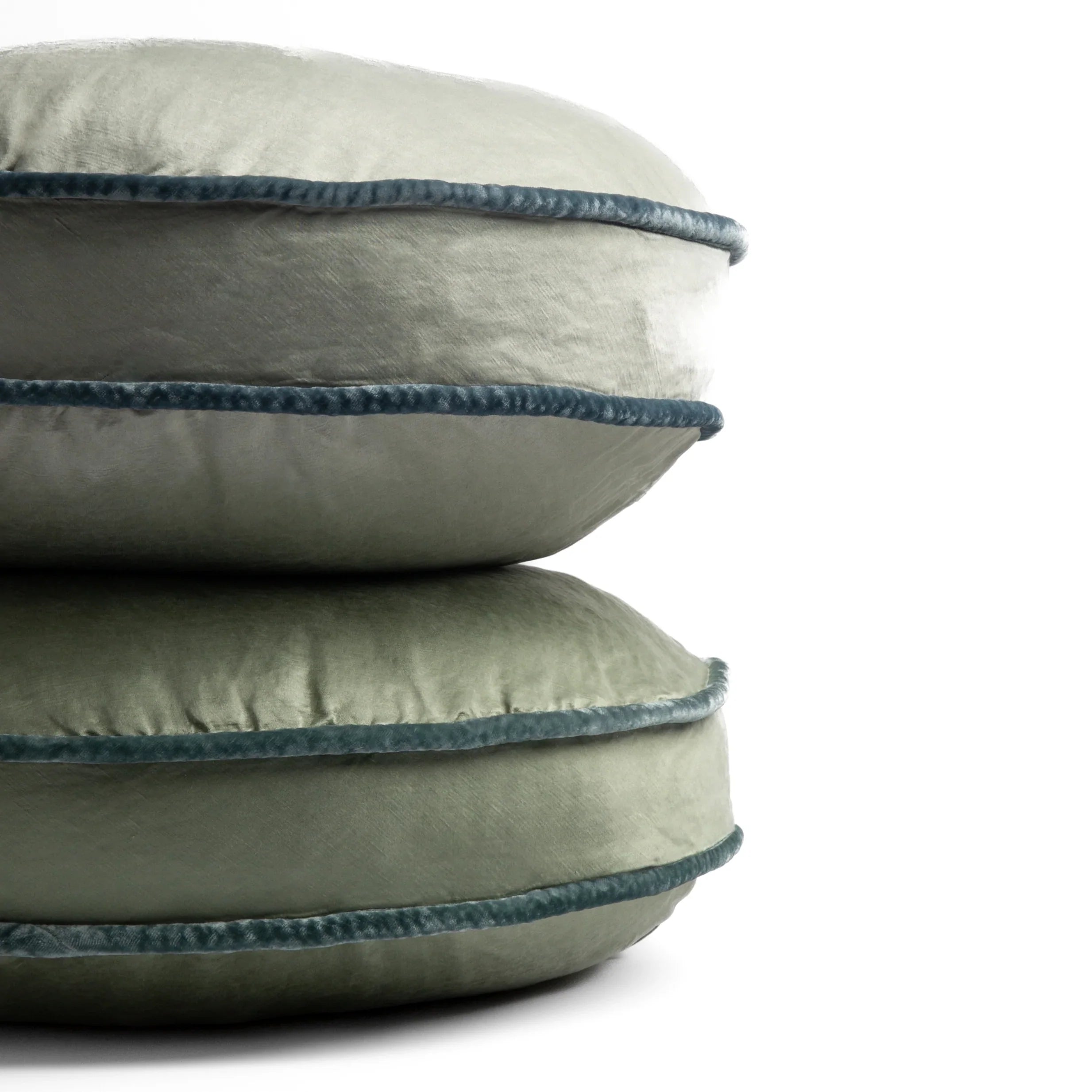 : two 18-inch round pillows stacked against a white background, showing the silk velvet trim on the pillow gussets — Mineral and Eucalyptus.