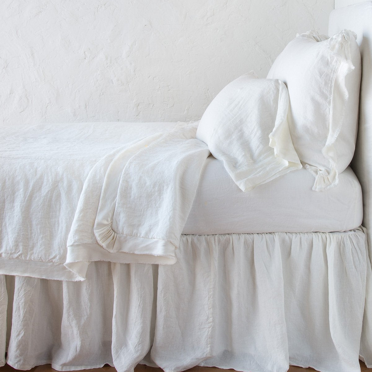 Winter White: satin trimmed linen coverlet on monochromatic bed with corner pulled back to reveal sheet, bed skirt - side view.