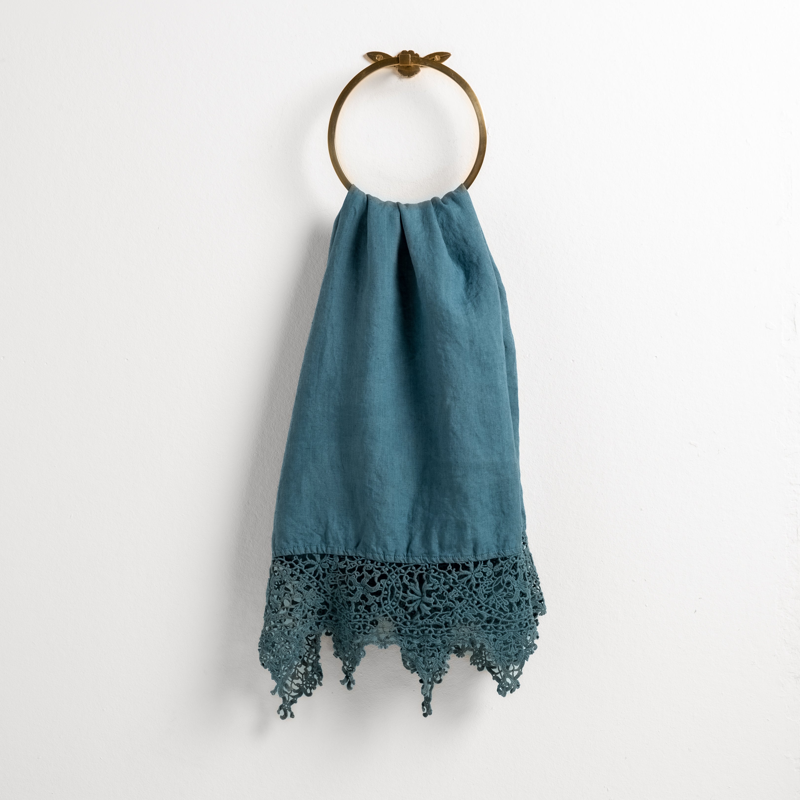 Cenote: Lace trimmed linen guest towel draped through a decorative towel ring against a plain white background.