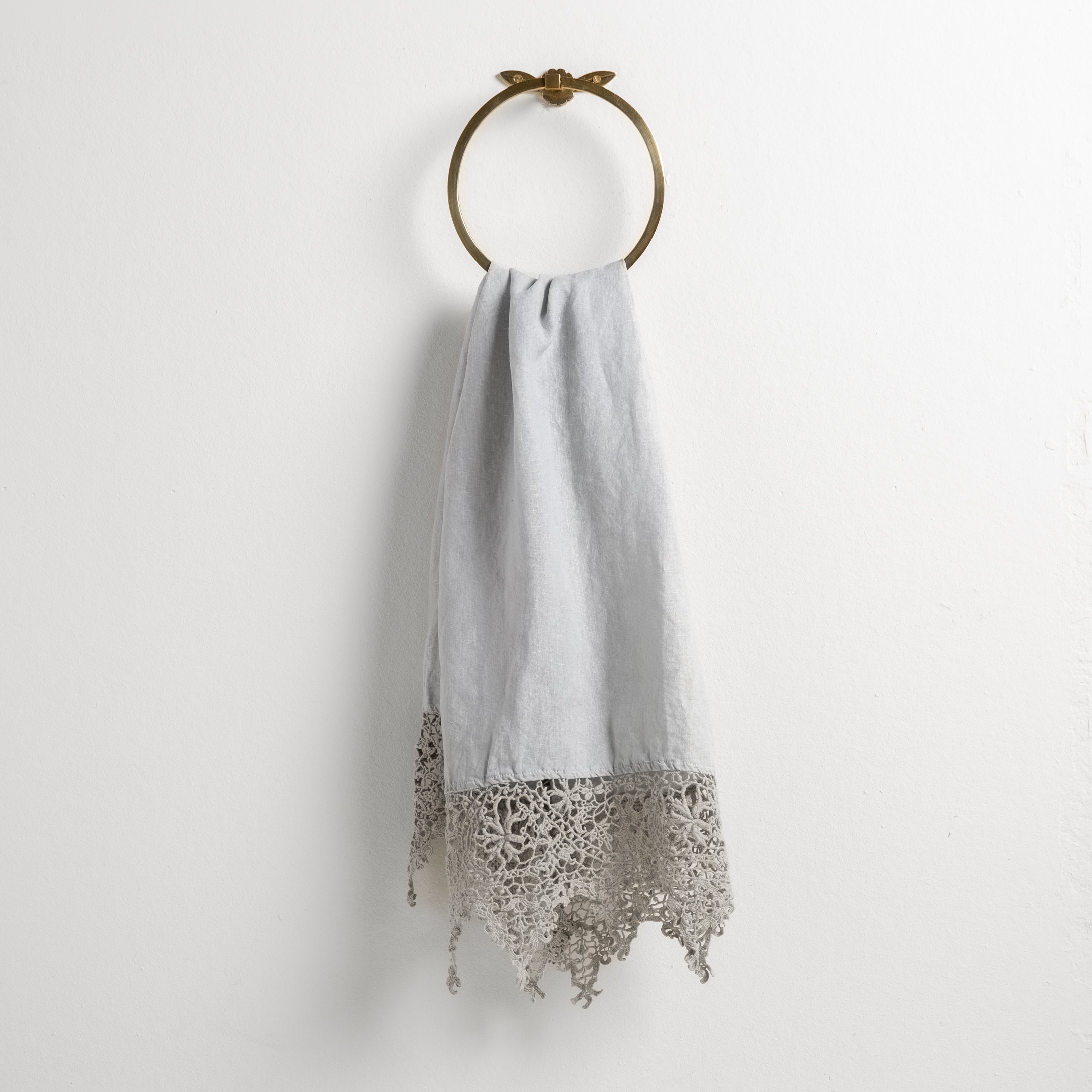 Cloud: Lace trimmed linen guest towel draped through a decorative towel ring against a plain white background.