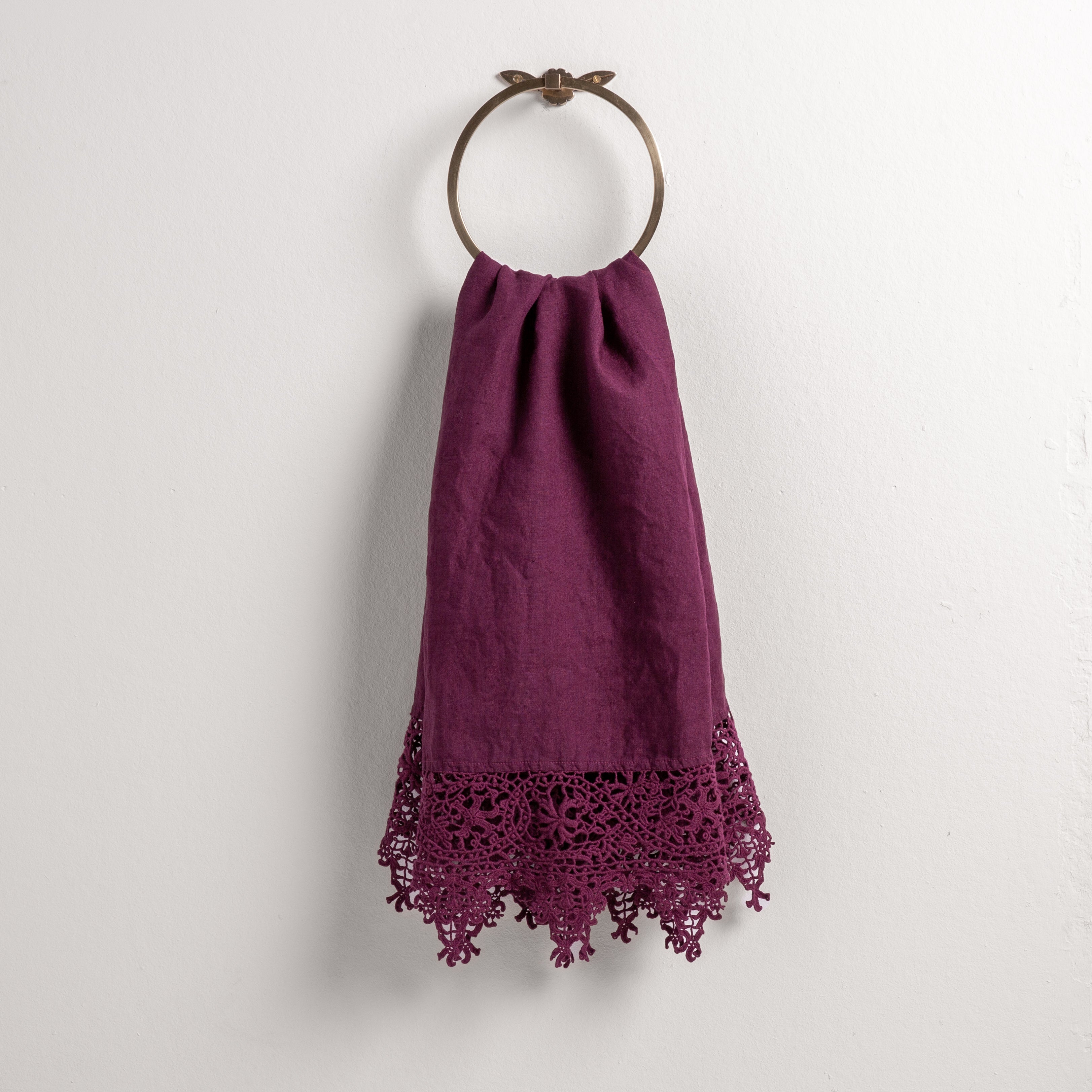Fig: Lace trimmed linen guest towel draped through a decorative towel ring against a plain white background.
