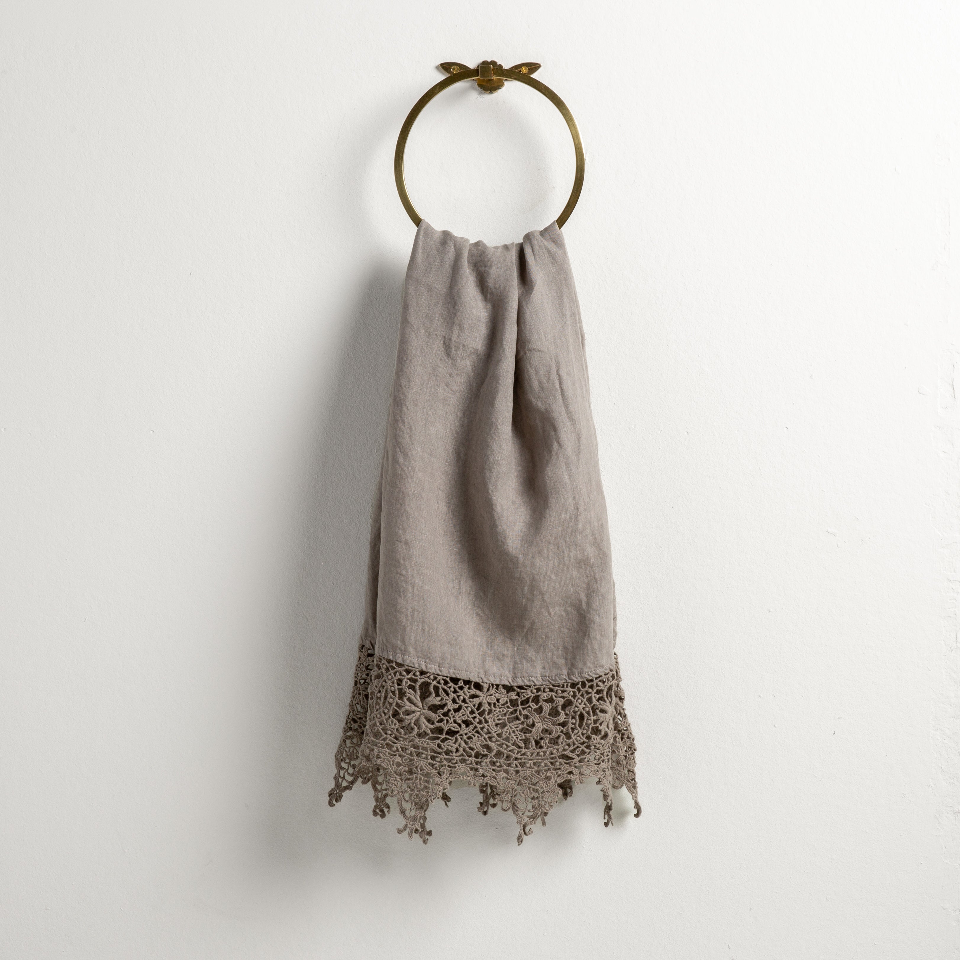 Fog: Lace trimmed linen guest towel draped through a decorative towel ring against a plain white background.