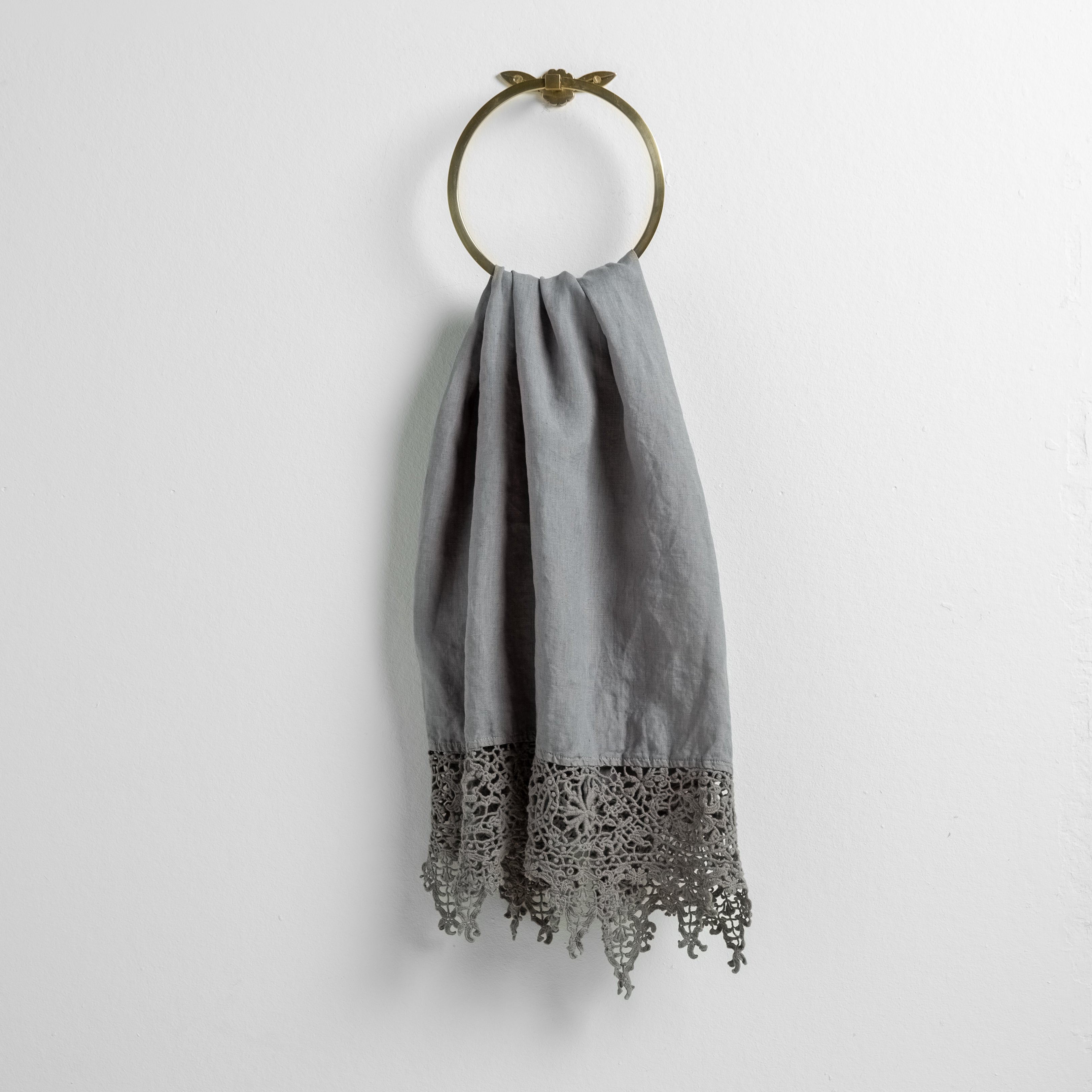 Moonlight: Lace trimmed linen guest towel draped through a decorative towel ring against a plain white background.