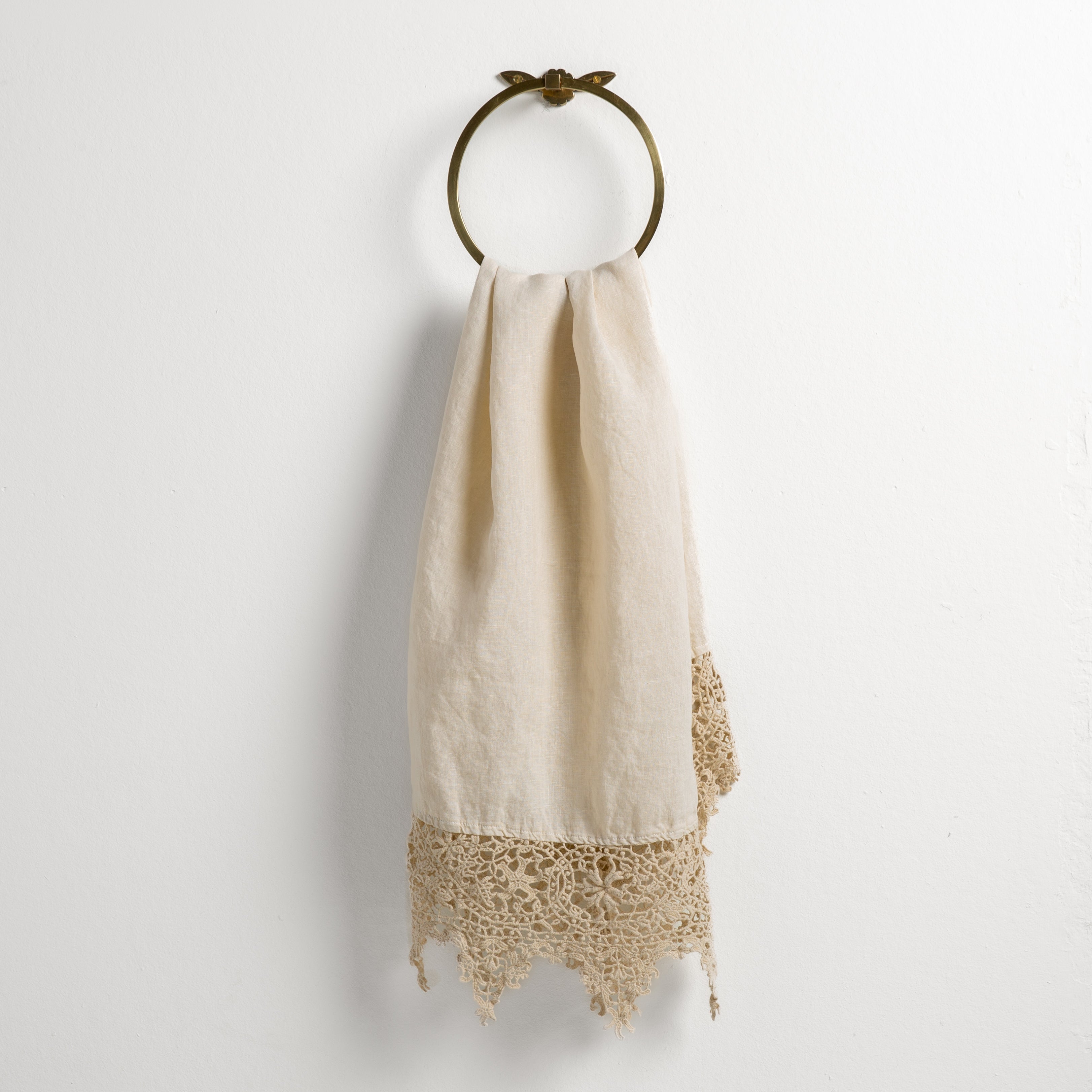 Parchment: Lace trimmed linen guest towel draped through a decorative towel ring against a plain white background.