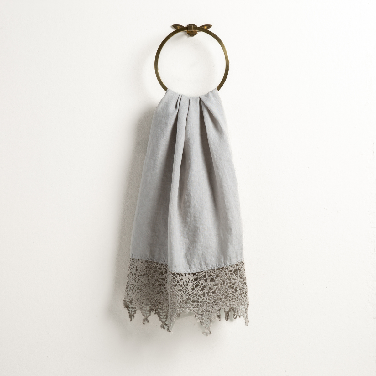 Sterling: Lace trimmed linen guest towel draped through a decorative towel ring against a plain white background.