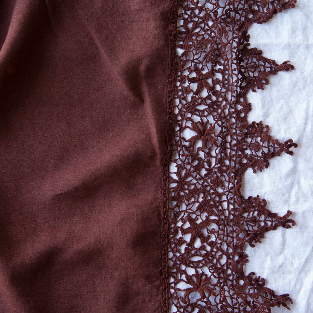 Mahogany: A close up of Frida, an antique cotton lace trim on a linen body, shown in mahogany, a deep, earthen, reddish brown.
