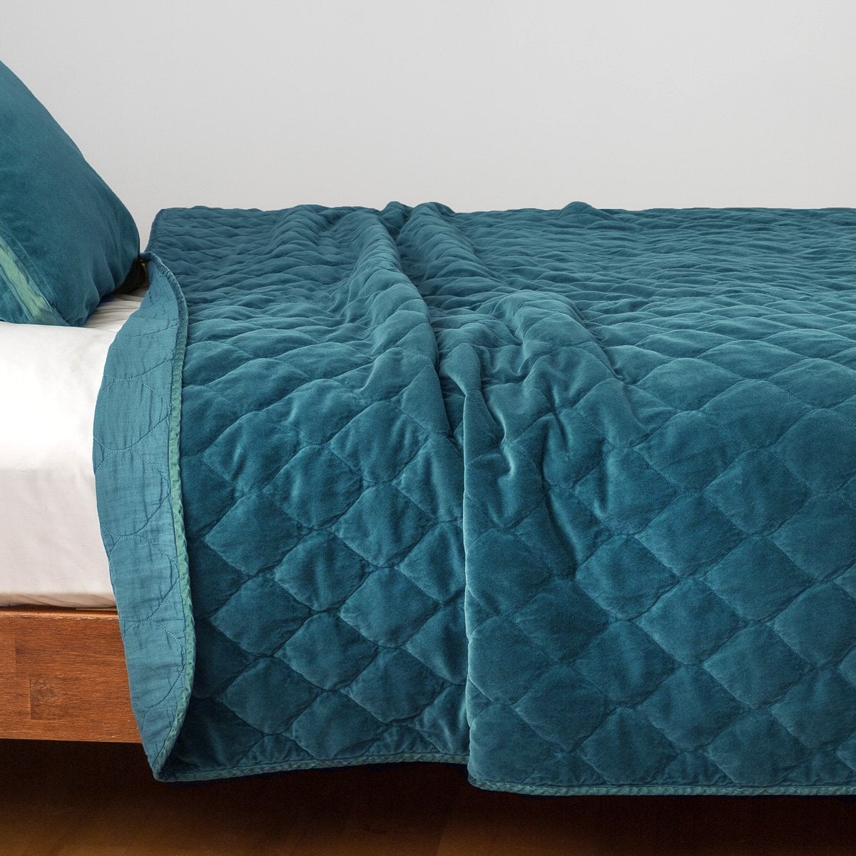 Cenote: Quilted cotton velvet coverlet, with top folded back to showcase linen back, draped over a white fitted sheet - side view.