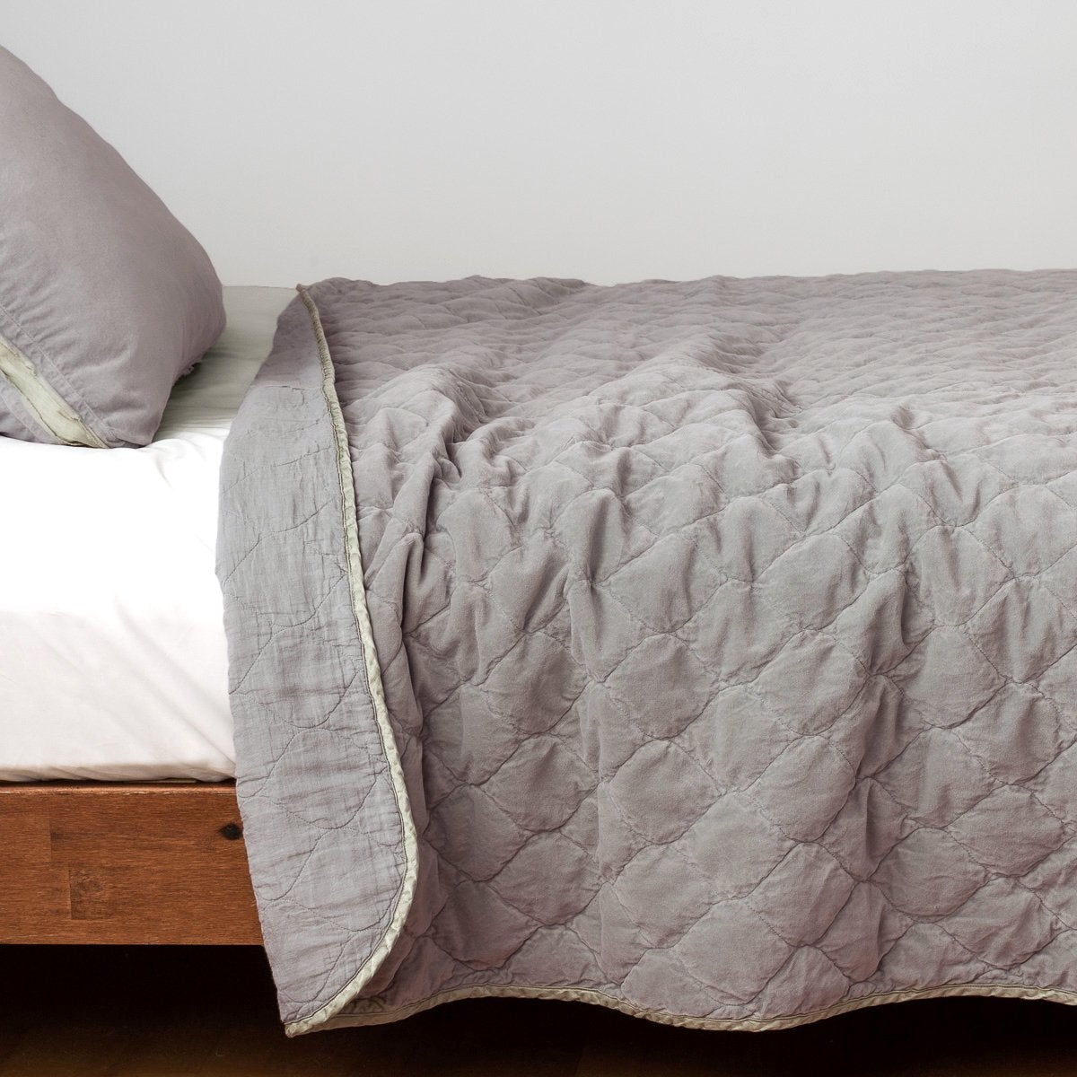 Fog: Quilted cotton velvet coverlet, with top folded back to showcase linen back, draped over a white fitted sheet - side view.