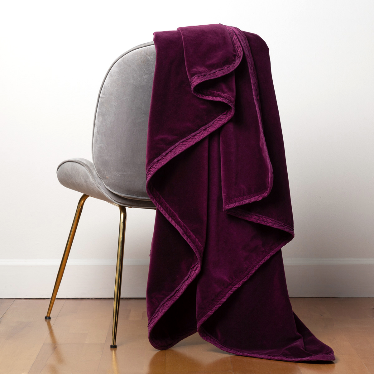 : Harlow throw blanket in fig draped over the back of a light grey chair, against a white wall and wood floor.