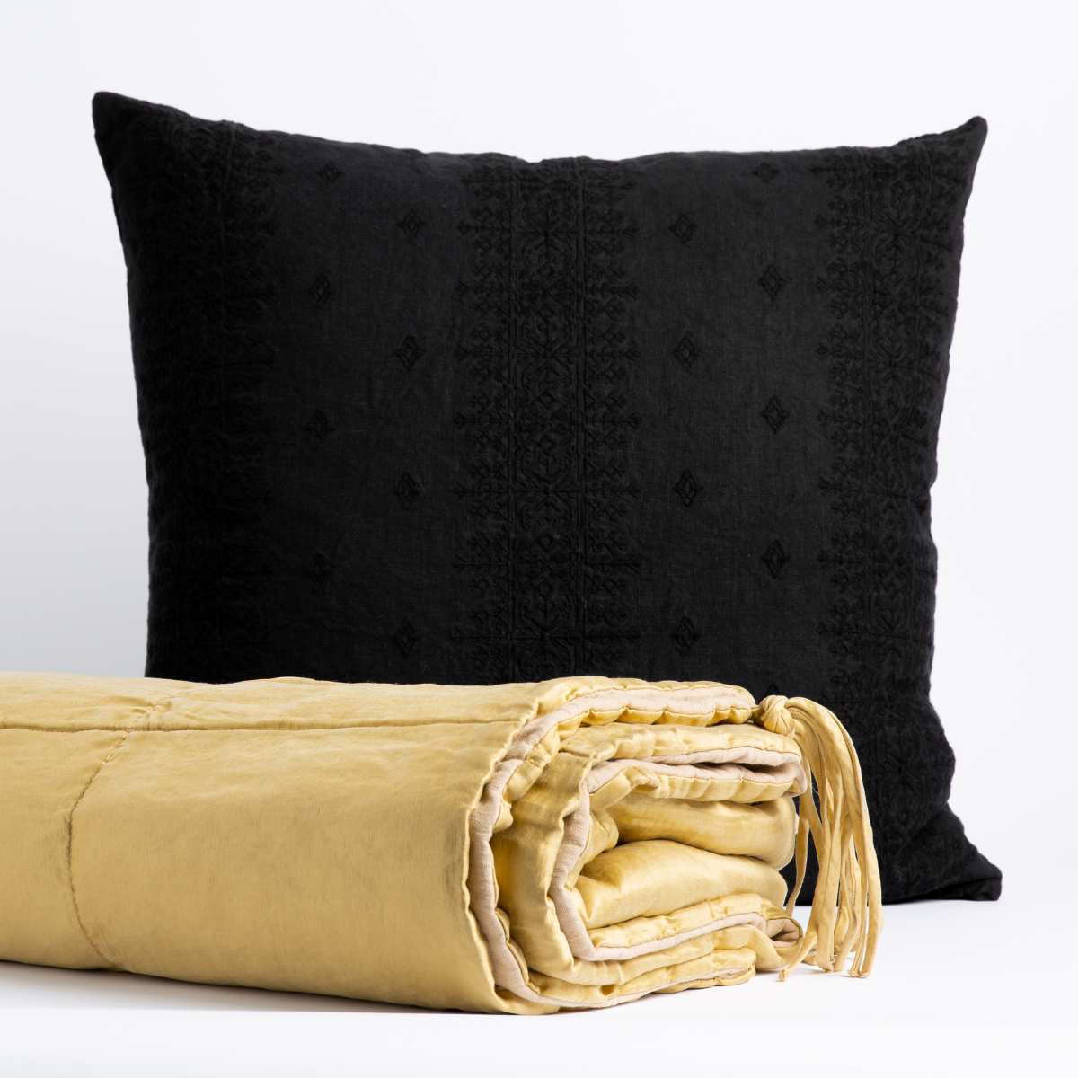 : Taline bed end blanket in honeycomb folded with tassel on corner showing against an ines throw pillow in corvino - front view with white background.