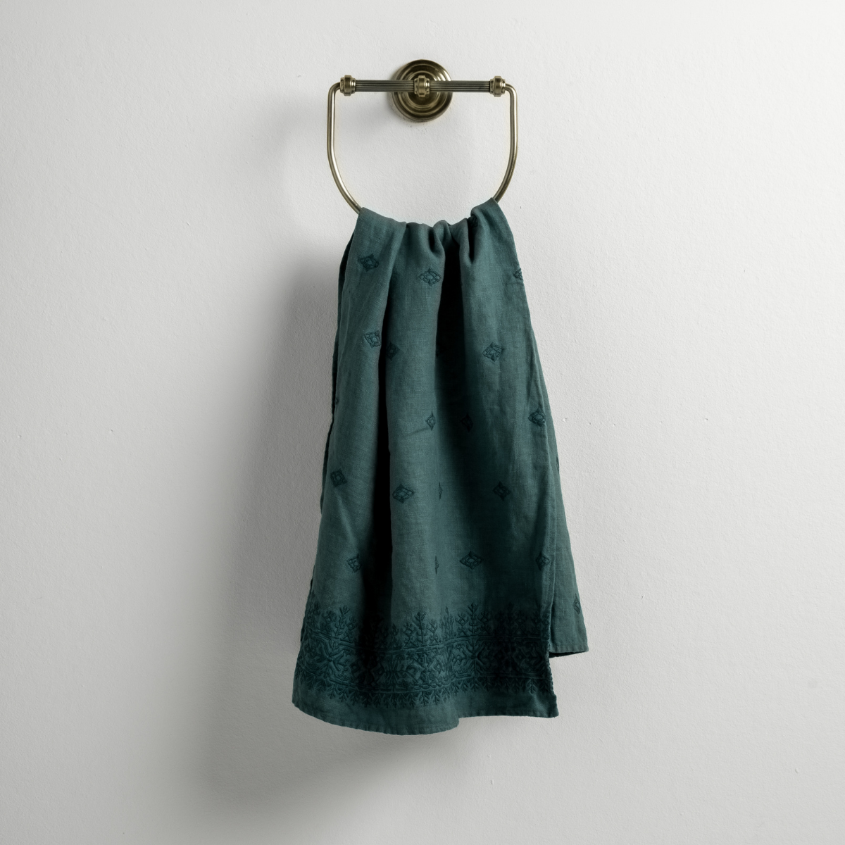Cenote: guest towel draped through a decorative brass towel ring against a white background.