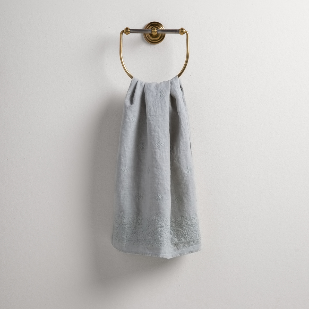 Cloud: guest towel draped through a decorative brass towel ring against a white background.