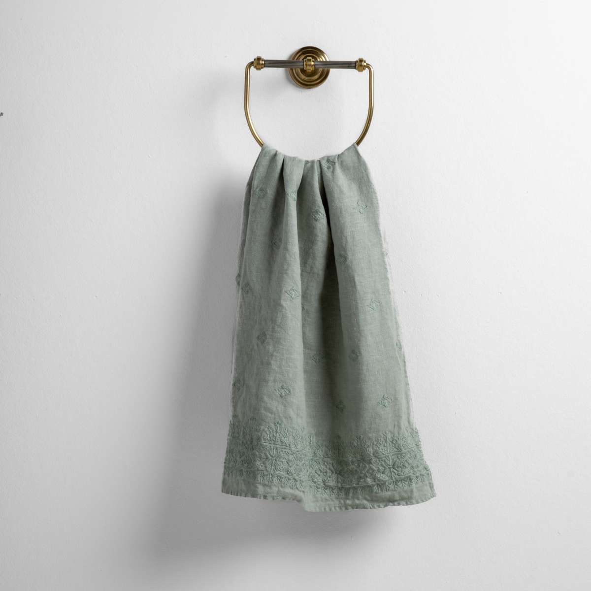 Eucalyptus: guest towel draped through a decorative brass towel ring against a white background.