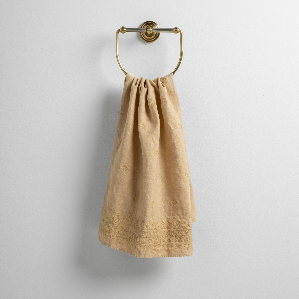 Honeycomb: guest towel draped through a decorative brass towel ring against a white background.