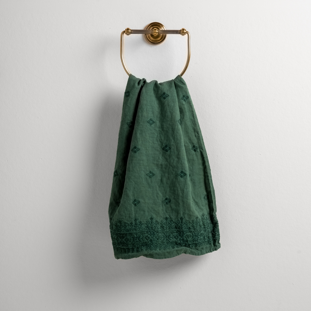 Jade: guest towel draped through a decorative brass towel ring against a white background.