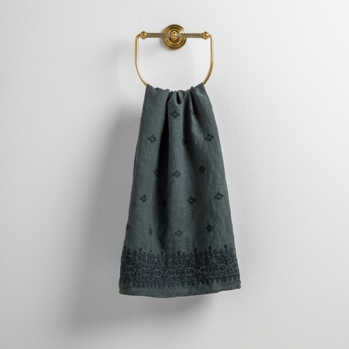 Midnight: guest towel draped through a decorative brass towel ring against a white background.